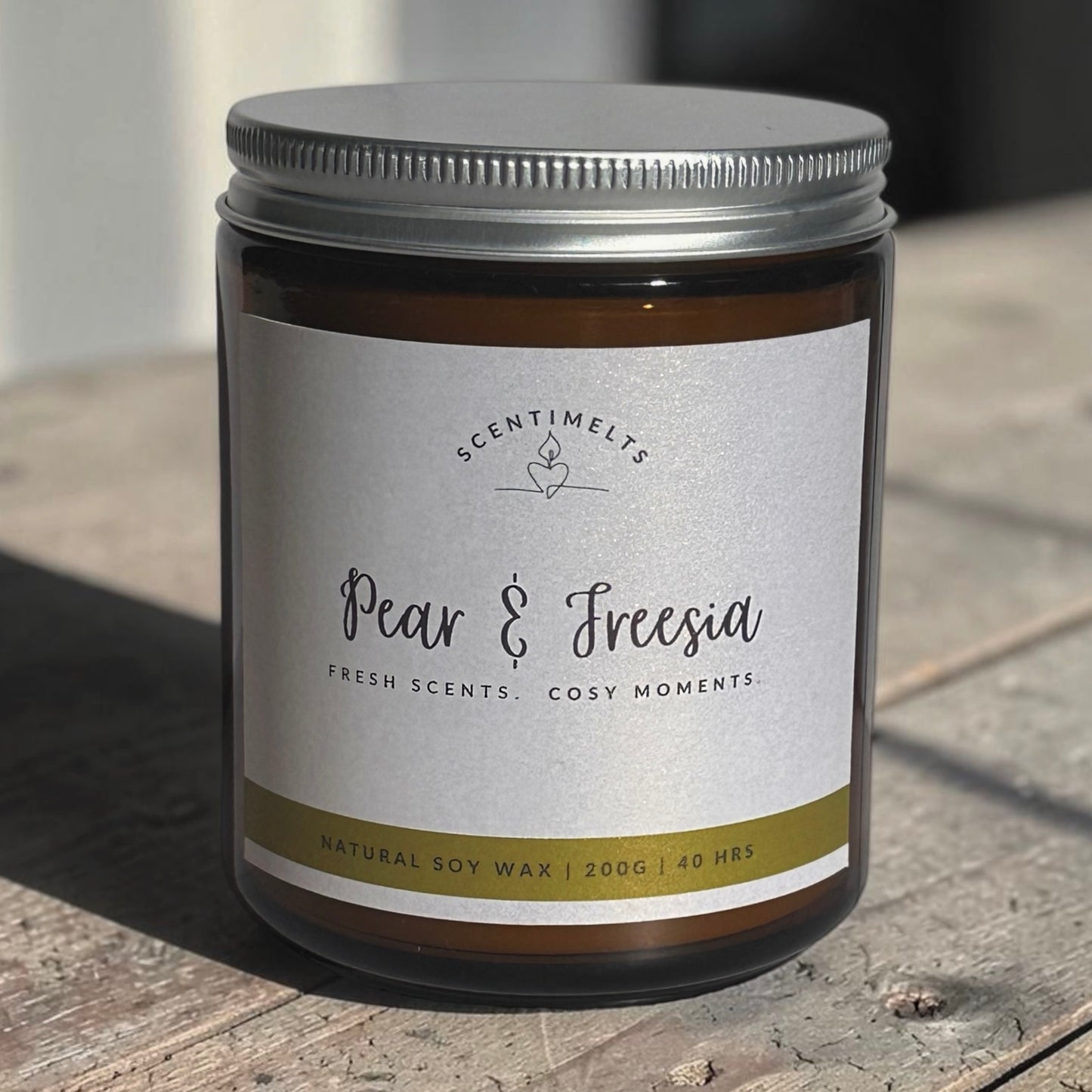 Candle jar labeled 'Pear & Freesia' by Scentimelts on a wooden surface.
