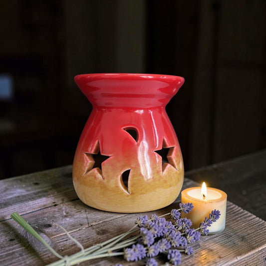 Red and beige ceramic oil burner with star cutouts on a wooden surface with a lit candle and lavender.