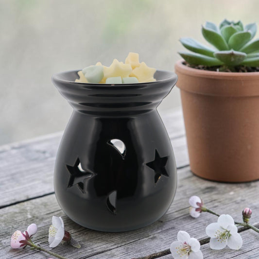 Black ceramic wax melt burner with moon and star cut-outs on a wooden surface