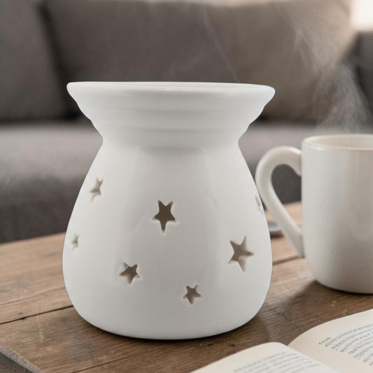 White ceramic wax melt burner with star cut-outs styled on a wooden table