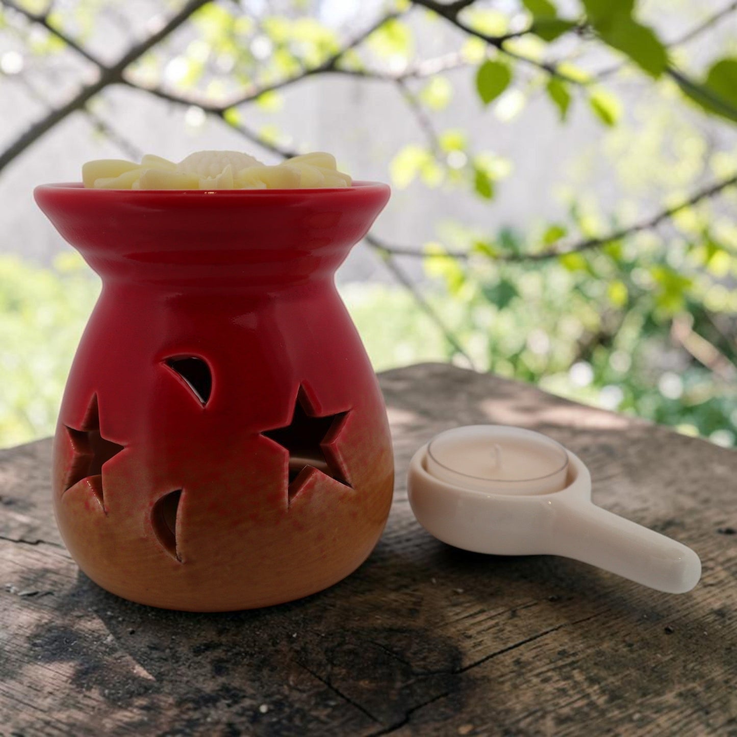 Red and gold ceramic wax melt burner with star cut-outs on a wooden surface